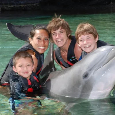 A happy family wearing wetsuits holding a dolphin in the pool.