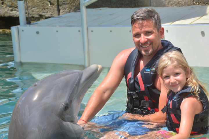 Father and daughter wearing wetsuits having dolphin experience in the pool.