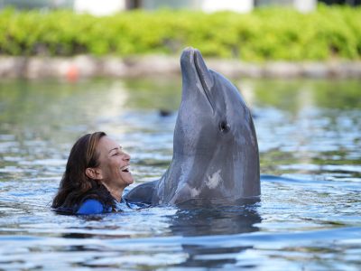 A woman enjoying and embracing a dolphin the pool.