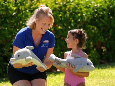 A little girl and a Dolphin Quest crew holding a dolphin stuffed toy.