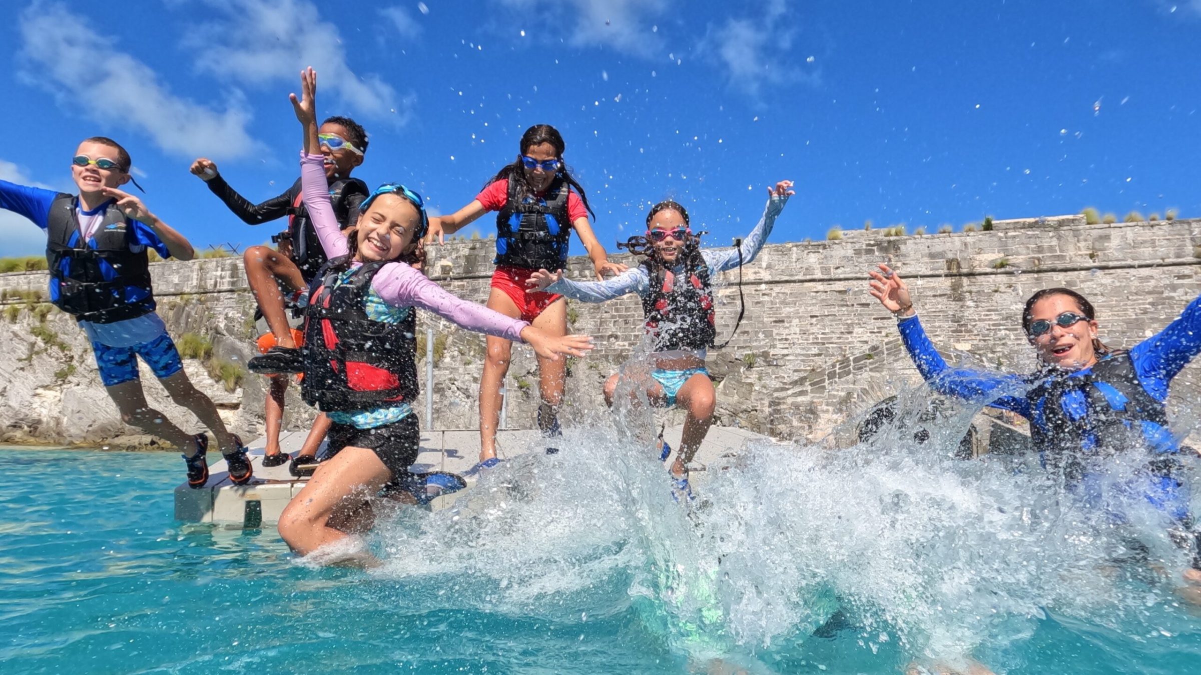 A group young children and a crew wearing wetsuits, enjoying their time on the pool.