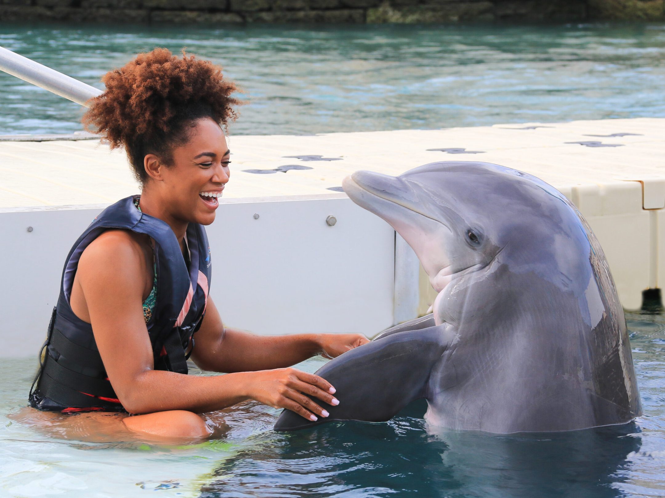 A woman in wetsuit smiling while interacting with a dolphin.