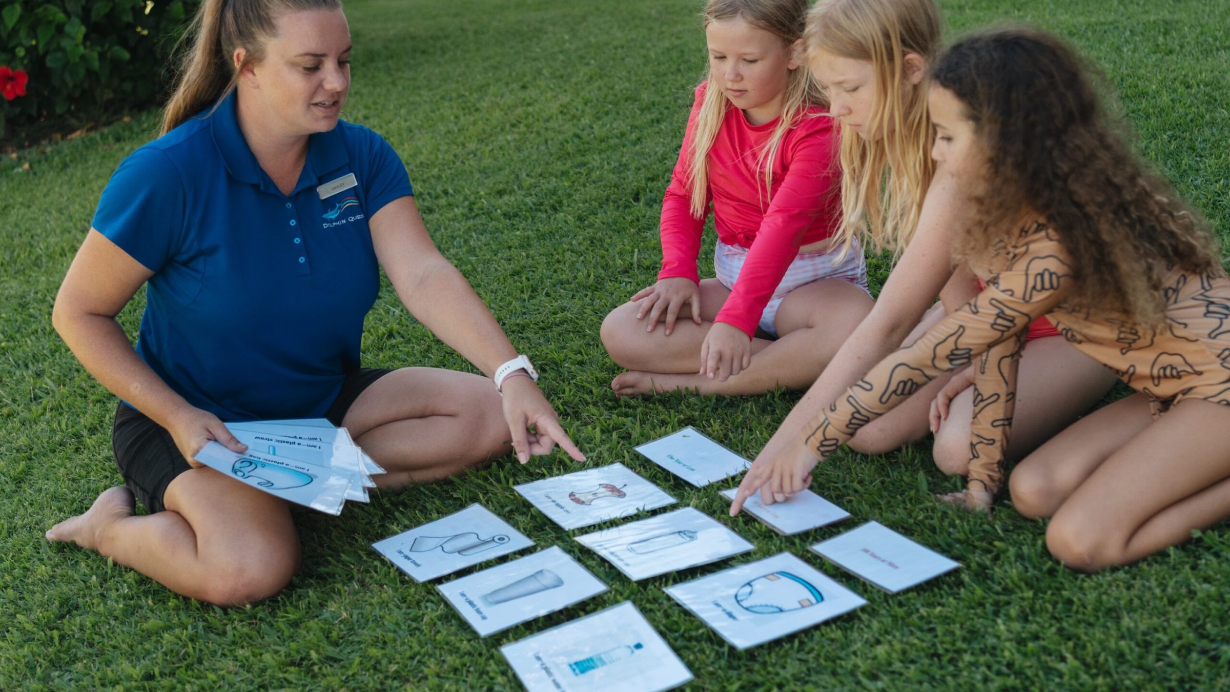 A group of young children sitting on the grass together with the Dolphin Quest crew having a lesson.