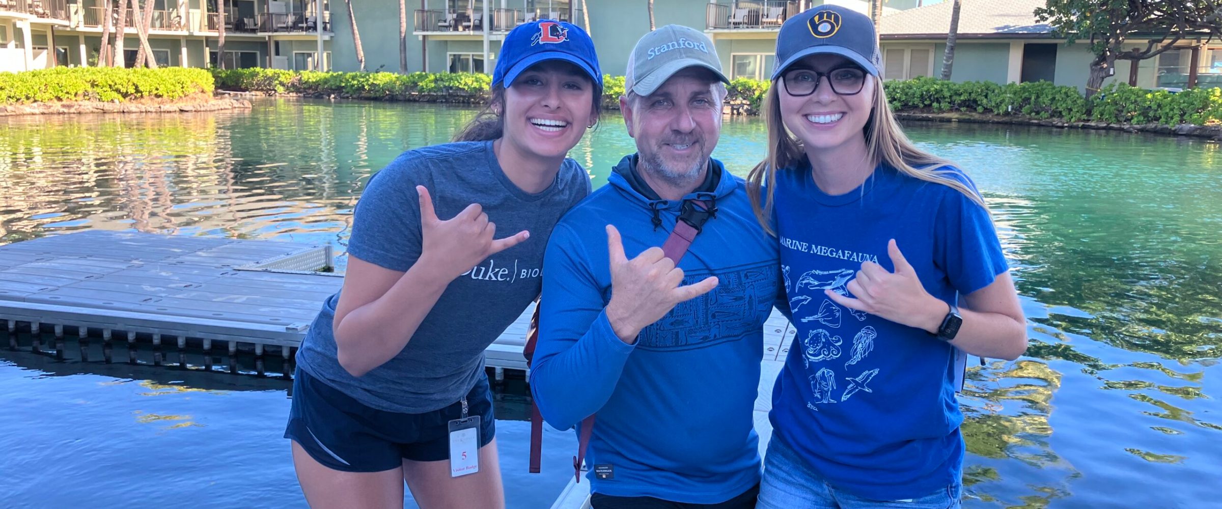 Three individuals smiling and posing for a photo on a wooden dock by the water. Three individuals smiling and posing for a photo on a wooden dock by the water.