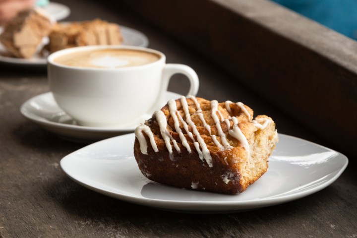 Cinnamon roll with icing on plate beside cup of coffee on a table.