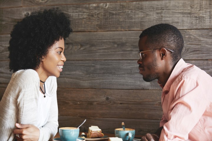 Two people sitting at a table, smiling and enjoying coffee and cake.
