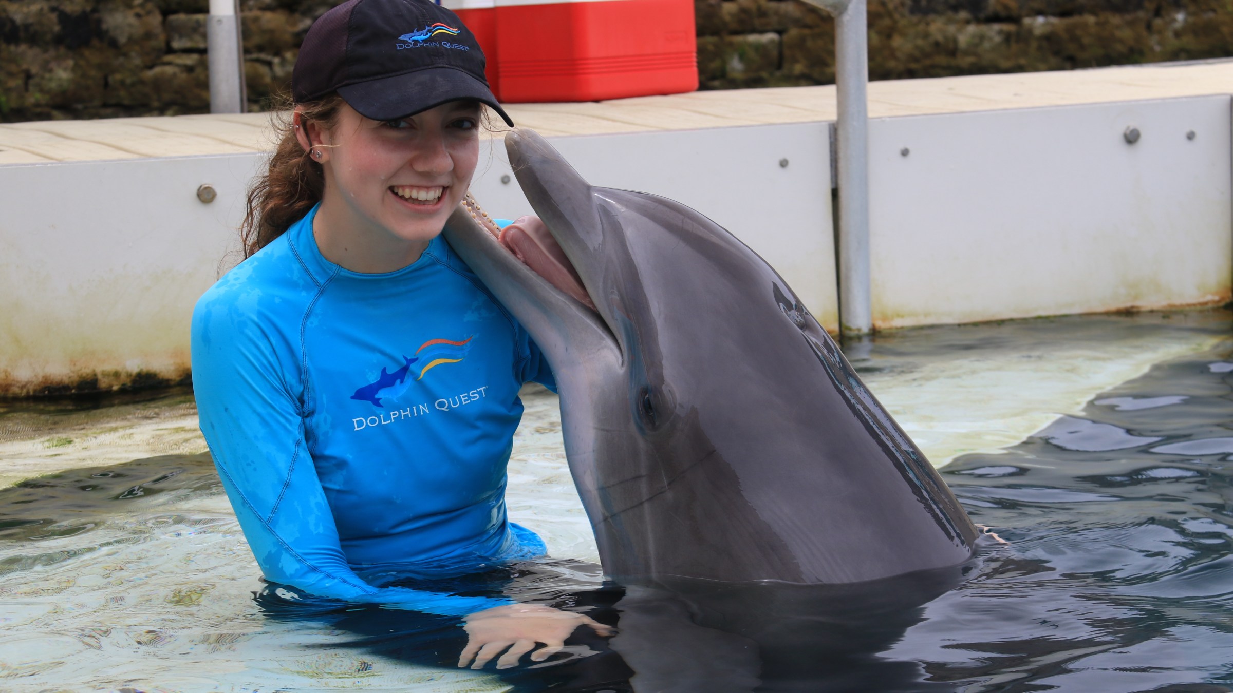 Woman in blue wetsuit with dolphin in water, both smiling.